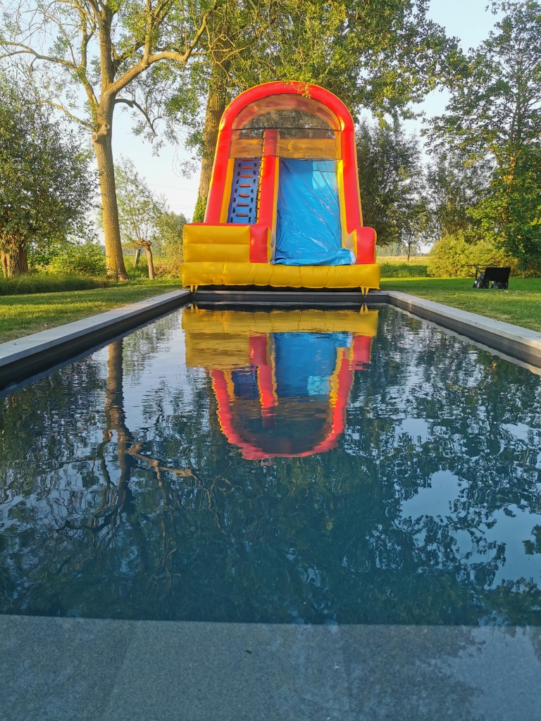 A large inflatable bounce house for children sits atop a rectangular swimming pool. The bounce house is predominantly yell...