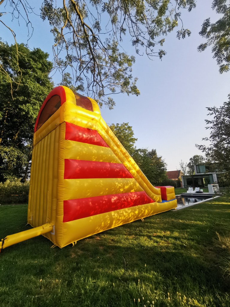 In the corner of a yard, a vibrant yellow and red bouncy house in the shape of a slide beckons children to come and play.