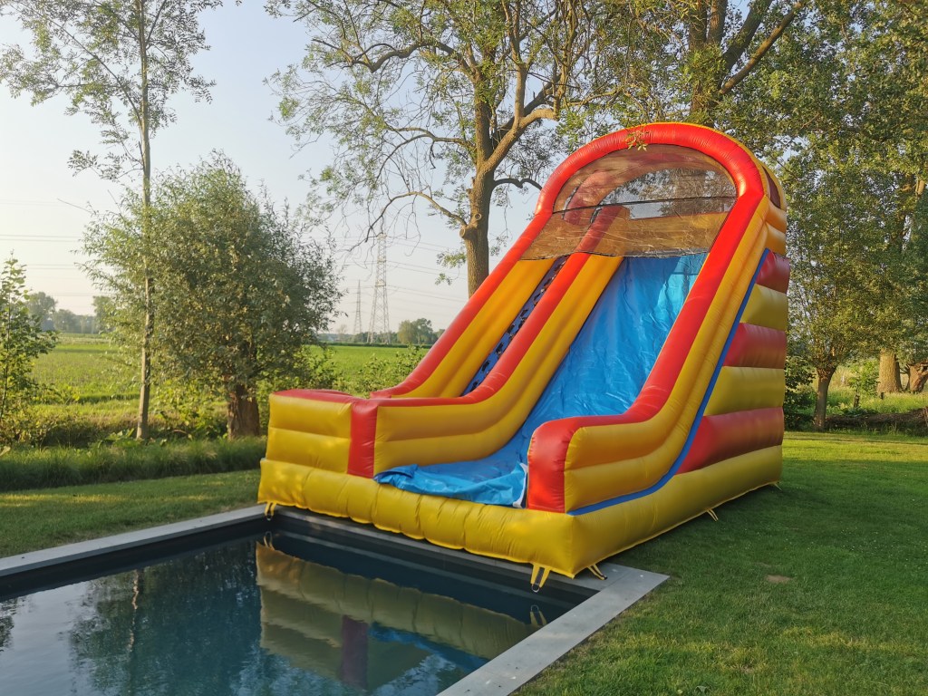 An inflatable slide sitting on the grass beside a pool, surrounded by trees.