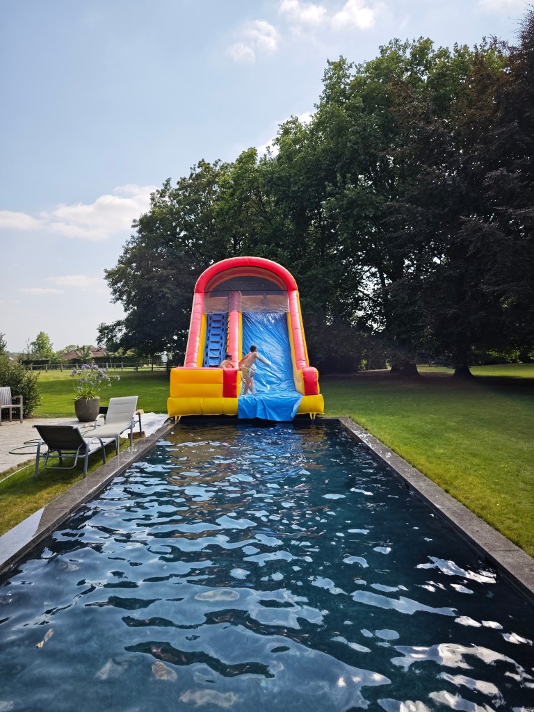 [large inflatable bounce house with slide in backyard next to a pool]